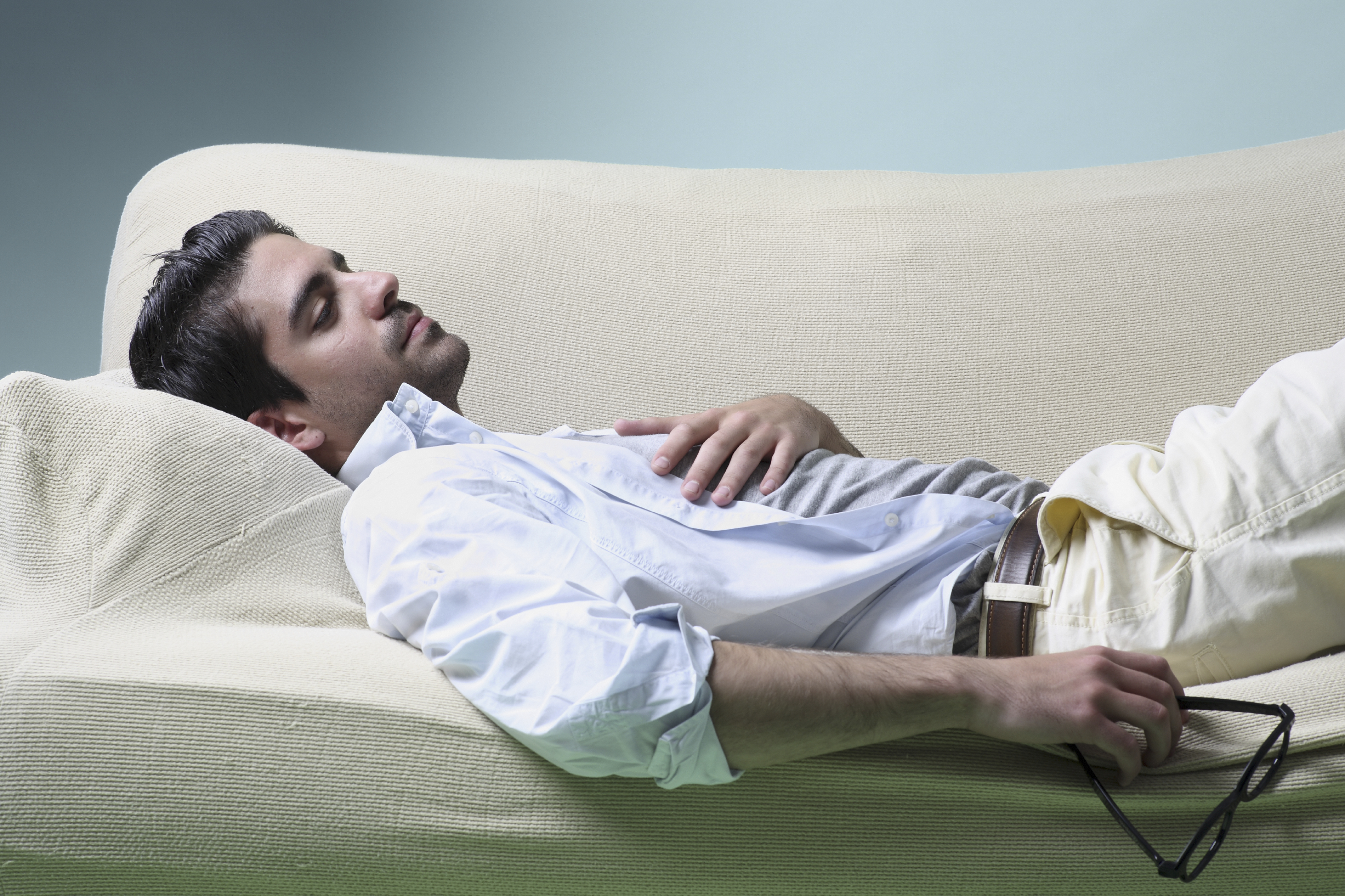 One youn man resting, he is lying down on a sofa with a pair of glasses on his hand. Format: Horizontal Concept: life style, leissure and relaxation.