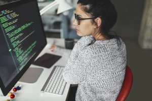 Photo of a young woman sitting at her desktop computer, doing computer programming in her home office