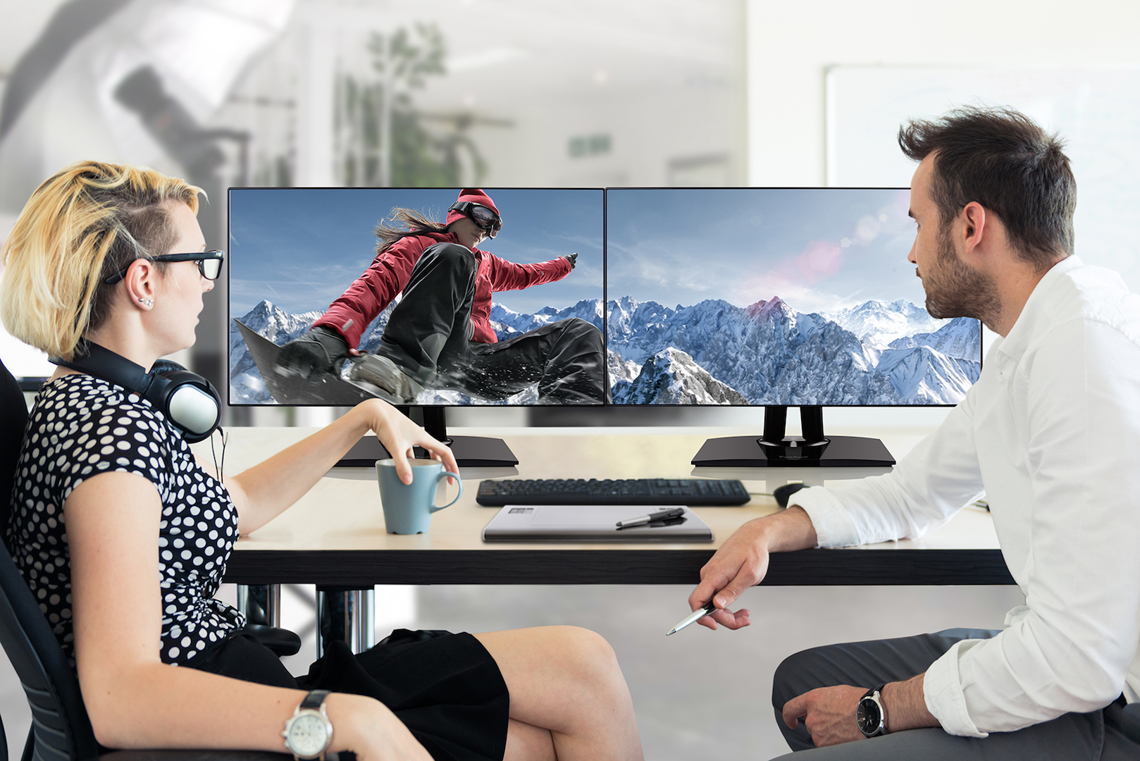 Casual dressed office workers talking about new project they are working on together. There is a blank monitor on the table between them.