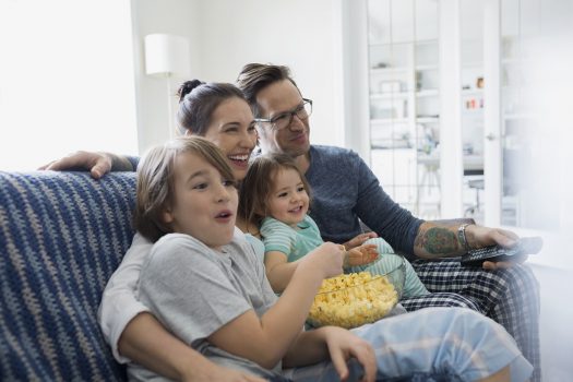 Family in pajamas watching TV and eating popcorn