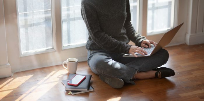 Close-up view of young female freelancer typing on laptop computer while sitting next to the windows