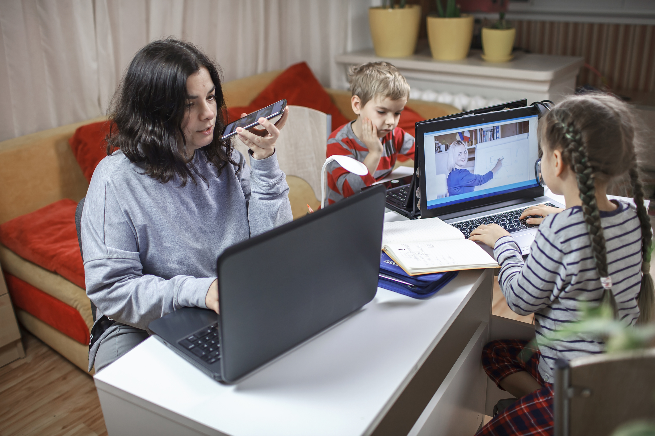 Kids doing homework and mother working online in one room, distant education at home