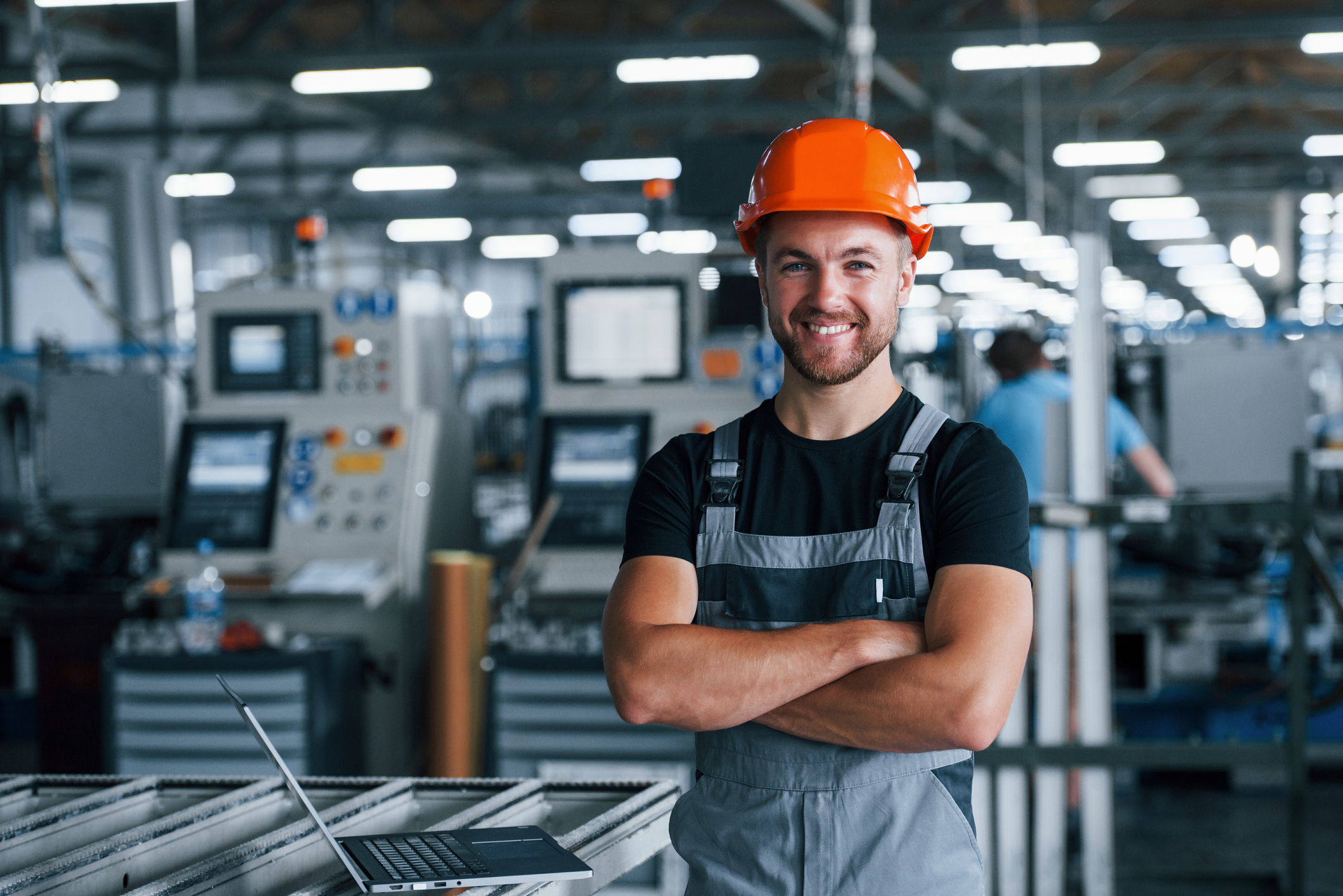 Smiling and happy employee. Industrial worker indoors in factory. Young technician with orange hard hat