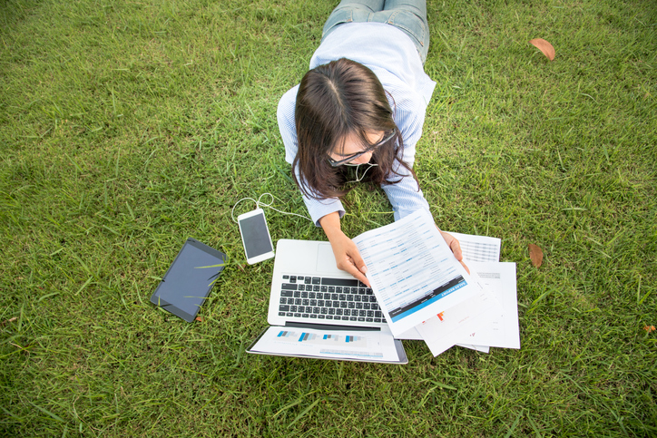 Asian woman lay down green garden park using laptop working outdoor home office. Happiness Woman smile working Freelance on laptop. Young Women University student type computer laptop at green nature