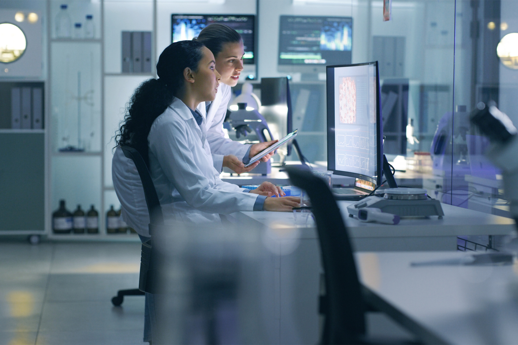 Focused, serious medical scientists analyzing research scans on a computer, working late in the laboratory. Lab workers examine and talk about results from a checkup while working overtime