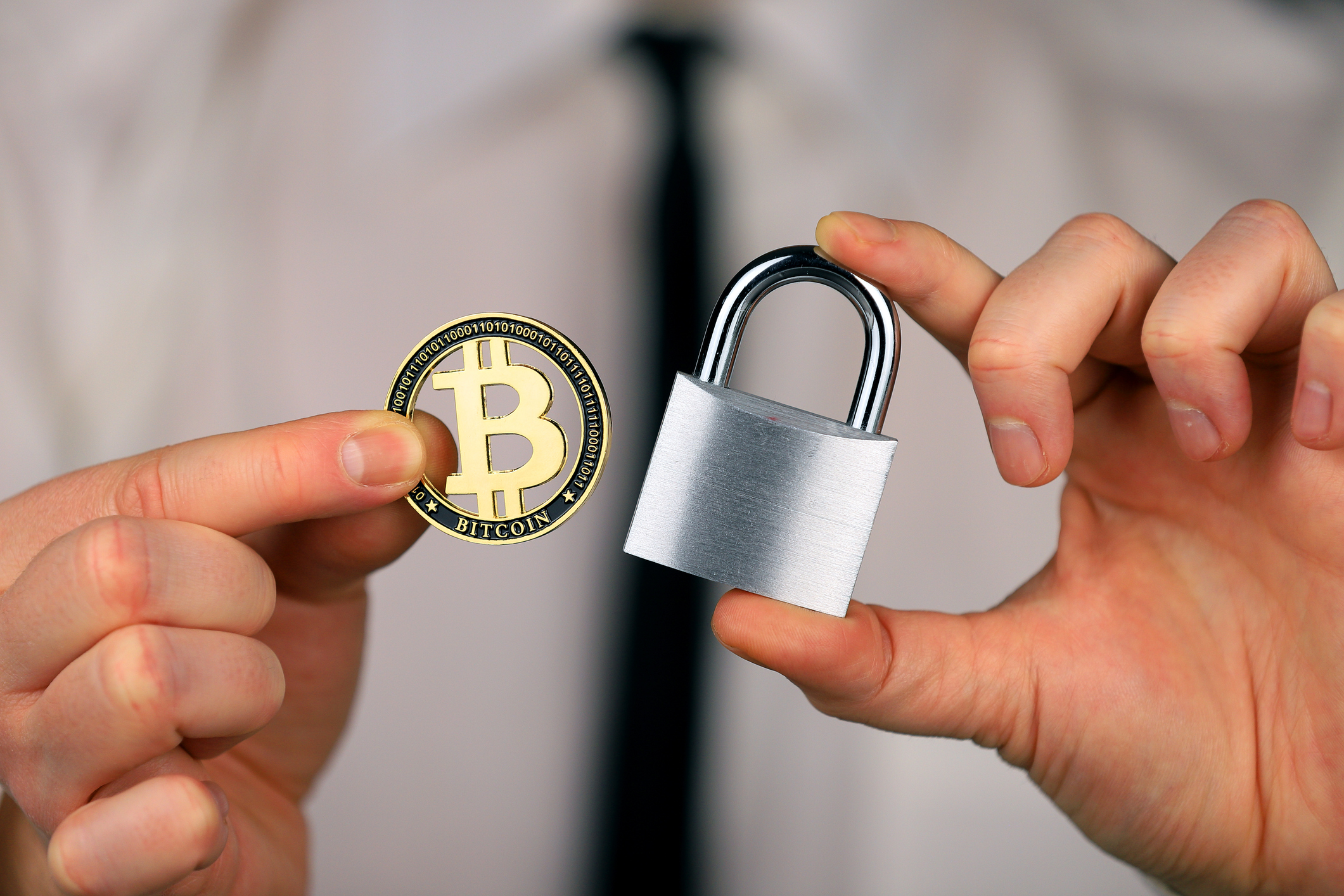 A businessman holds a silver padlock and physical version of bitcoin in his hands. Prohibition of cryptocurrencies, regulations, restrictions or security, protection, privacy