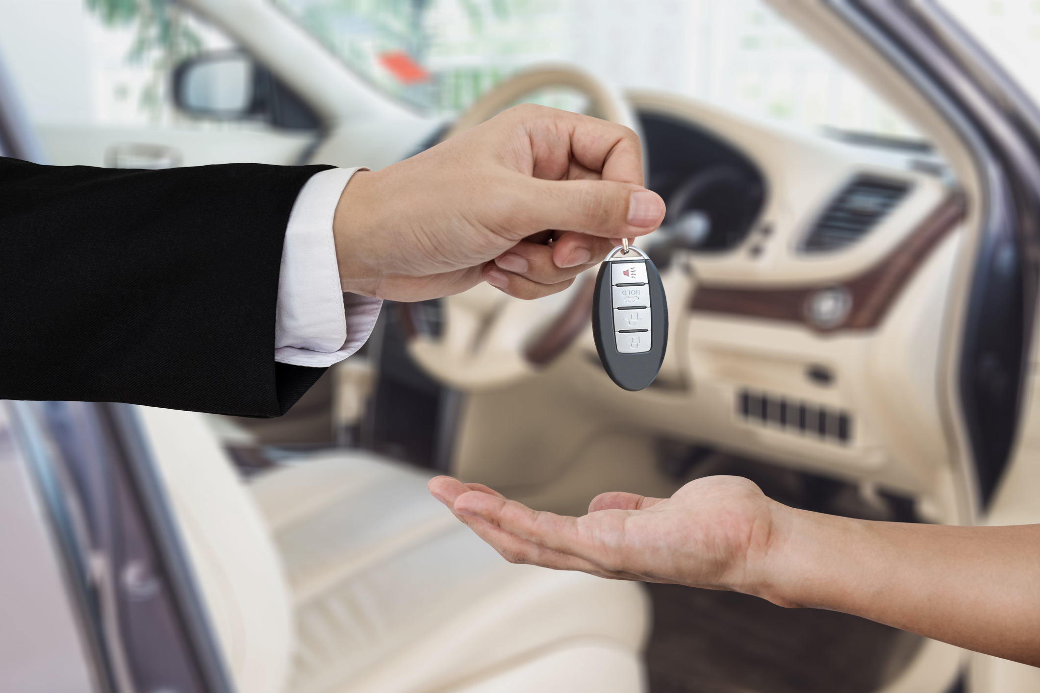 Hand giving and receiving car key remote, with modern car backgrounds