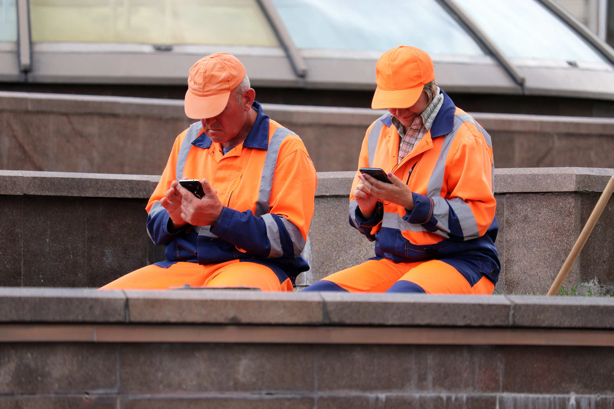Public utilities workers sitting with smartphones on a city street