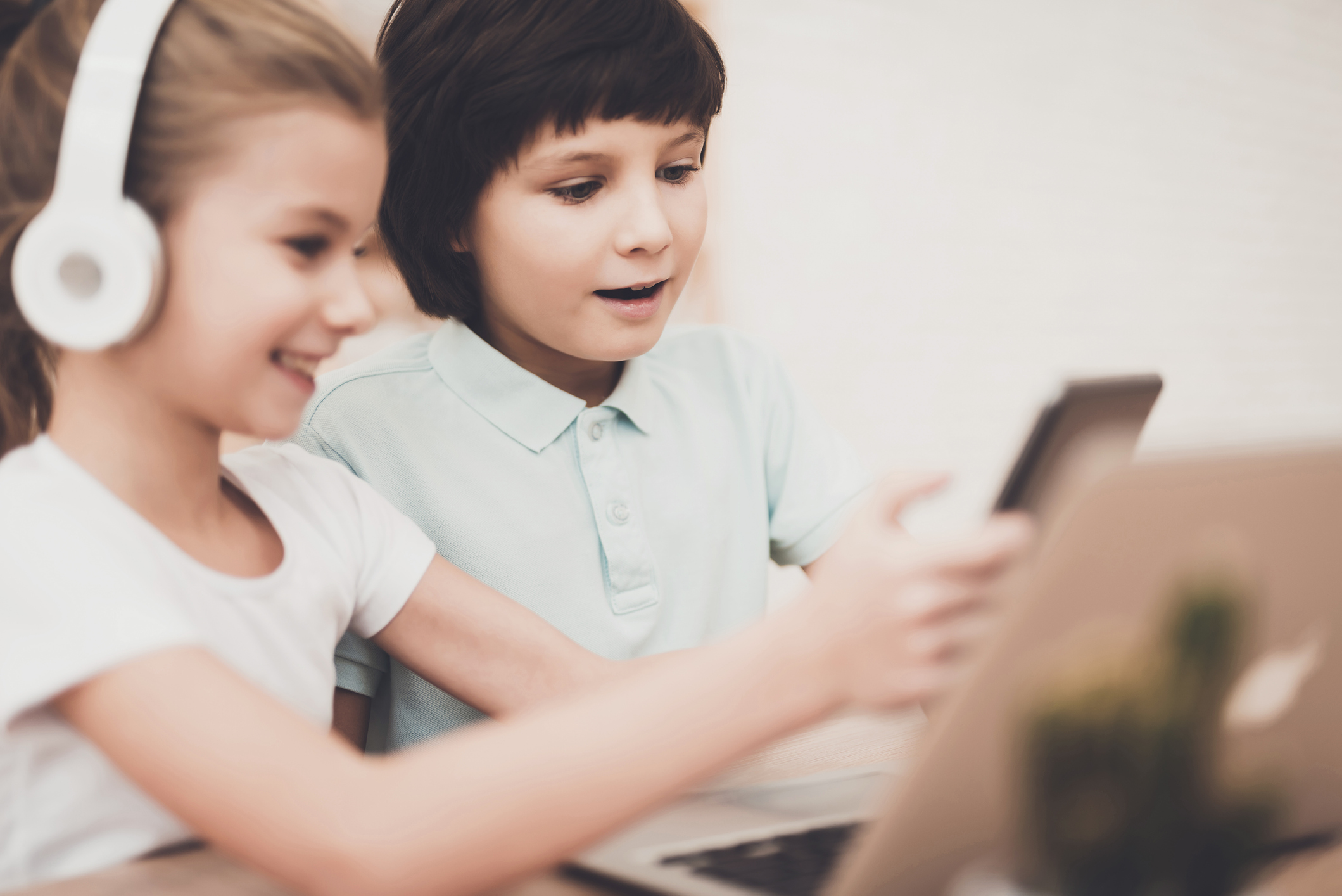 Children at home. Brother and sister are using tablet and laptop in headphones.